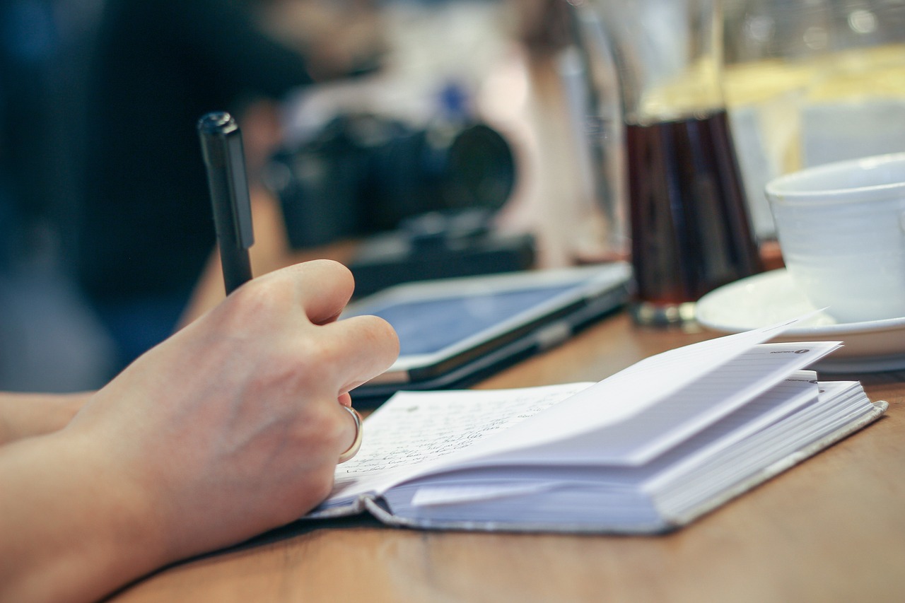 A hand writing in a notebook on a café table