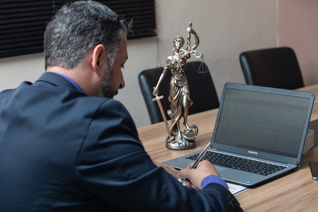 Lawyer at a desk with a Lady Justice figure A lawyer writing at a desk beside a laptop and a Lady Justice figurine